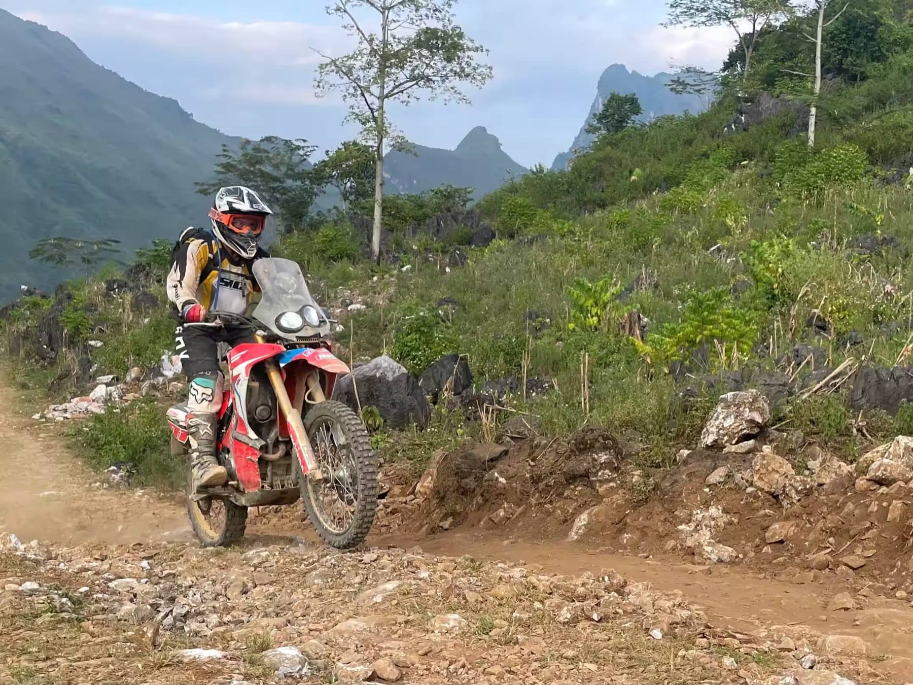 A guest rider on a dirt bike on a rocky hillside track among Ha Giang peaks