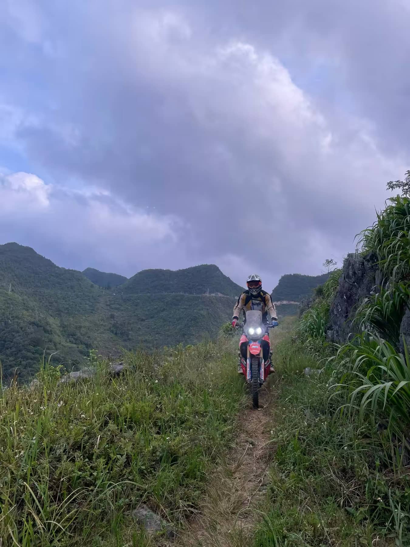 A guest riding a narrow grassy trail toward misty Ha Giang mountains