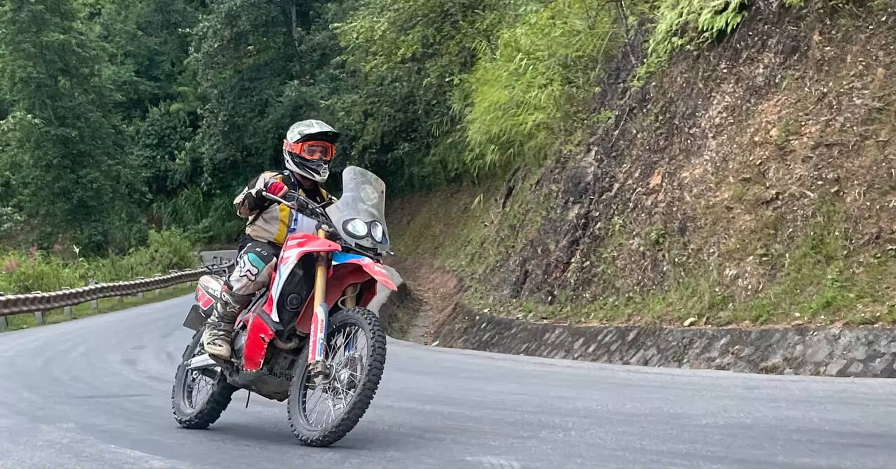 A guest riding a red dirt bike along a curving Ha Giang mountain road