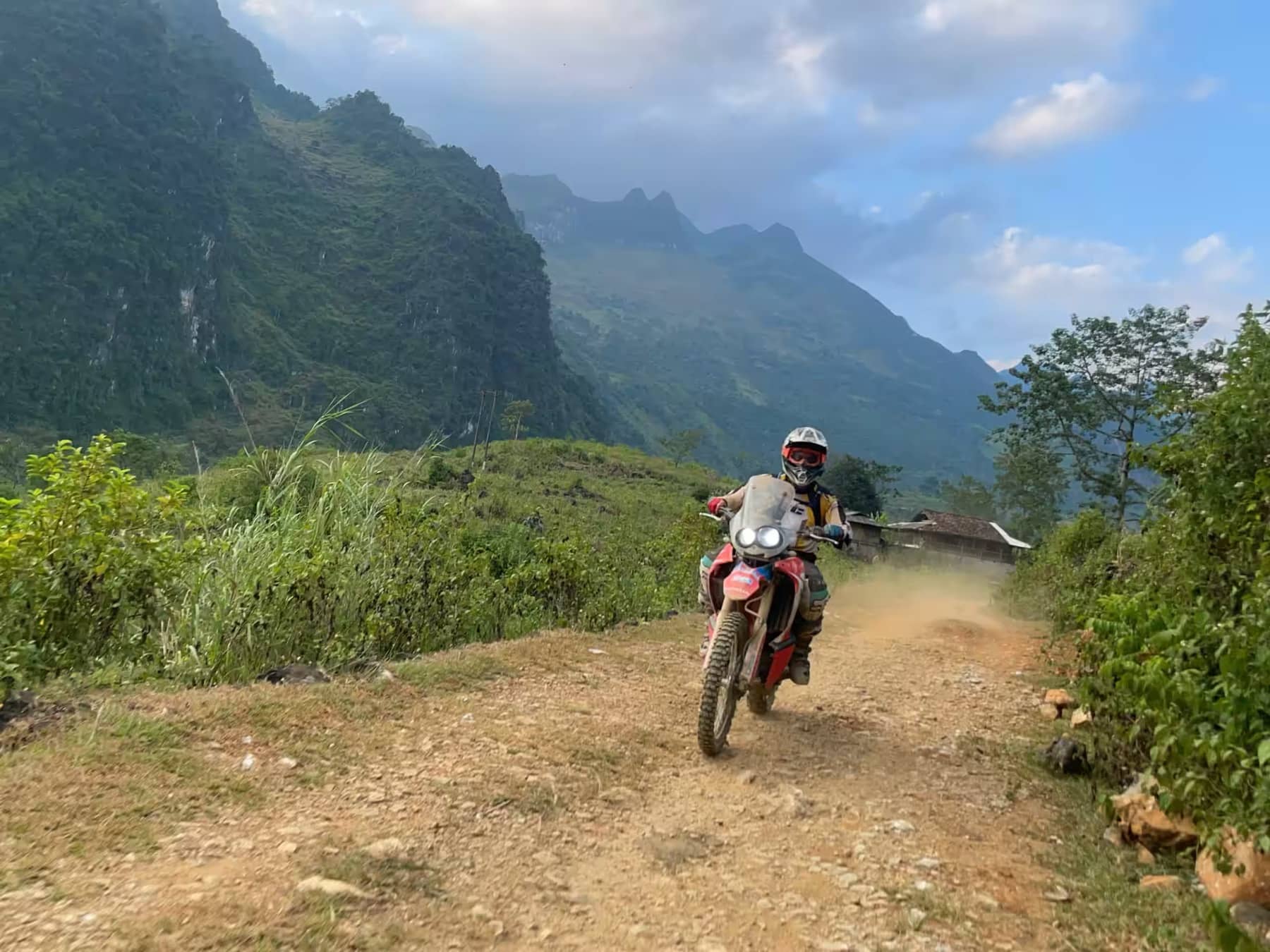 A guest riding a dirt track toward green karst mountains under a blue Ha Giang sky