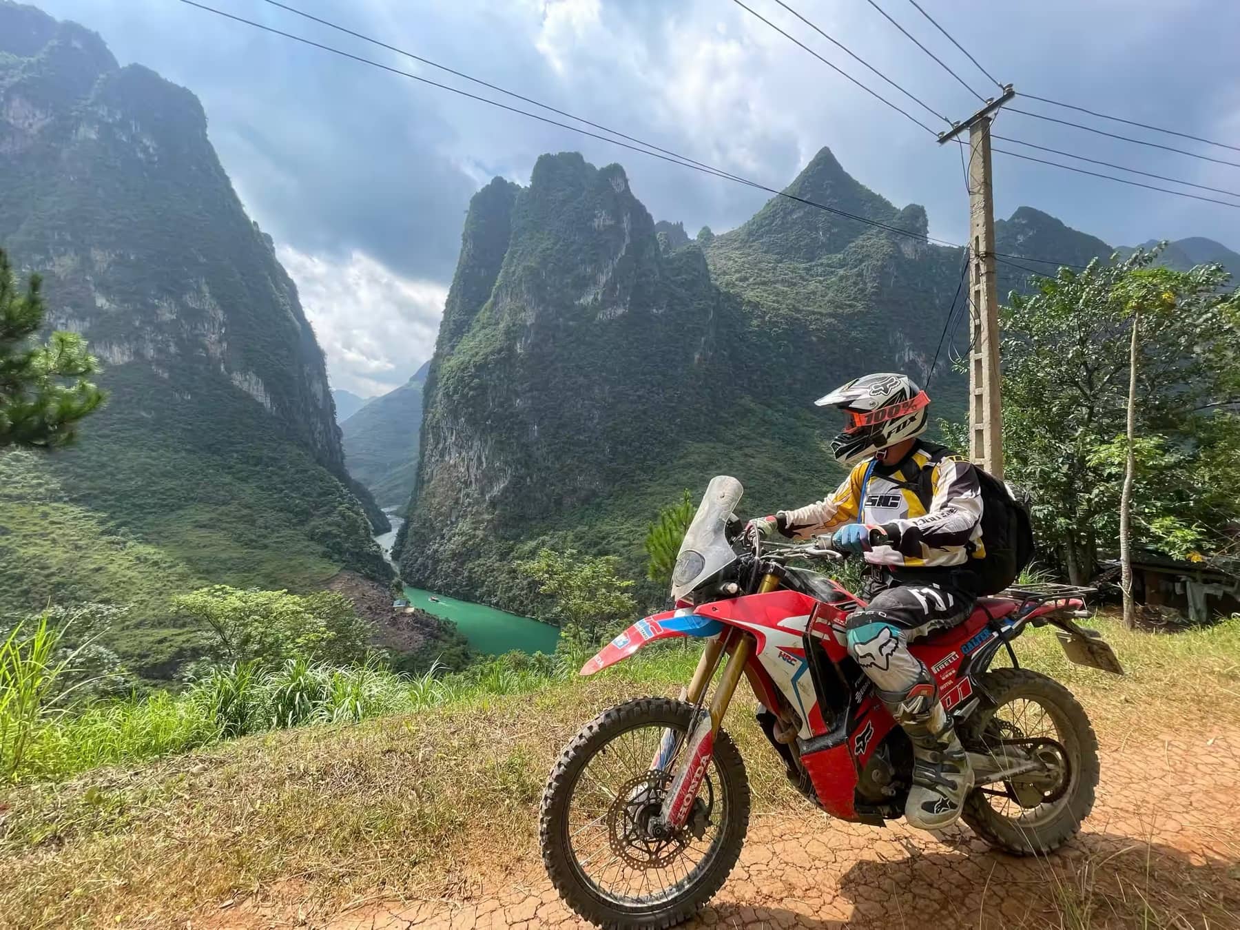 A guest on a red dirt bike above the turquoise Nho Que River and limestone cliffs in Ha Giang