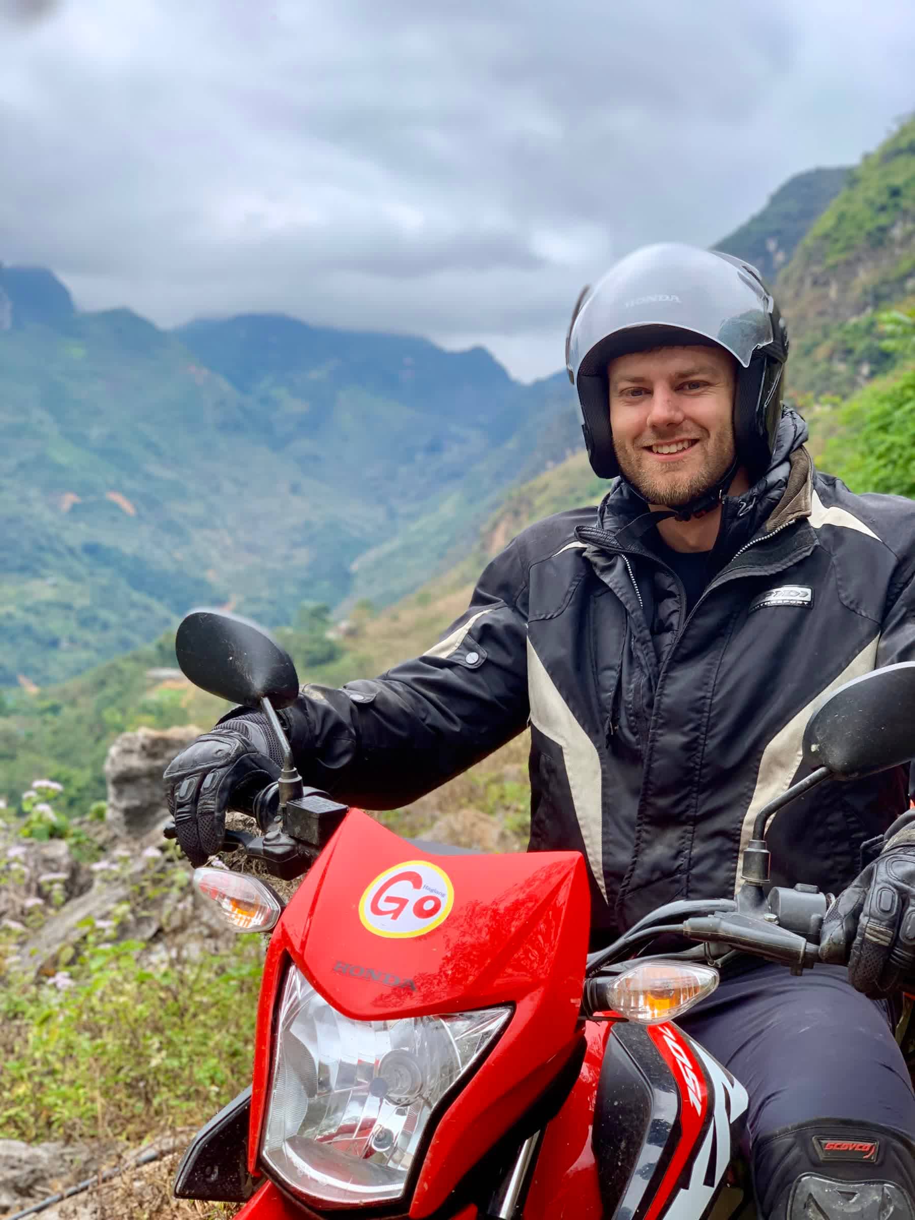 A guest rider standing with a red dirt bike above the terraced Ha Giang mountains