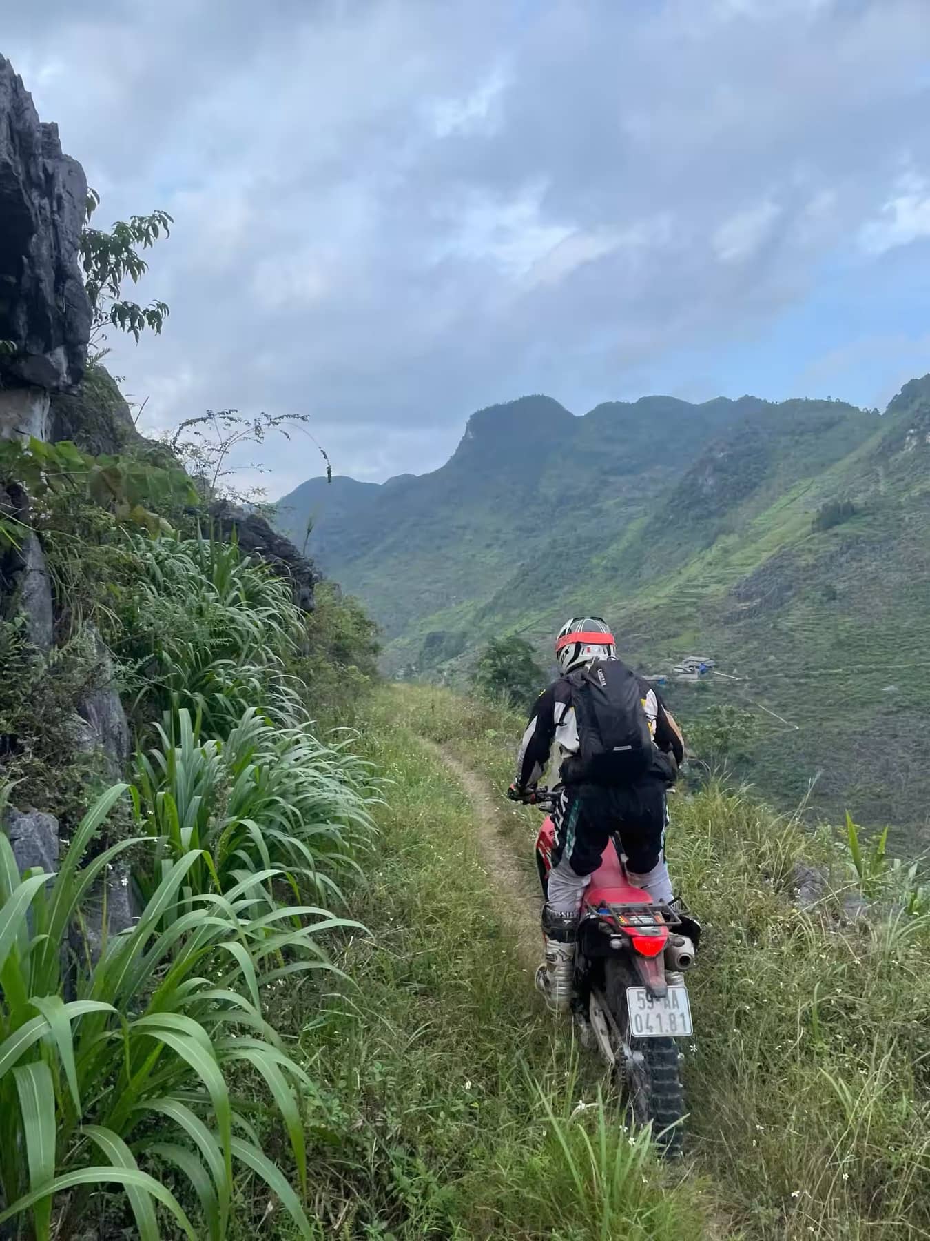 A guest riding away along a green ridge track high above a Ha Giang valley
