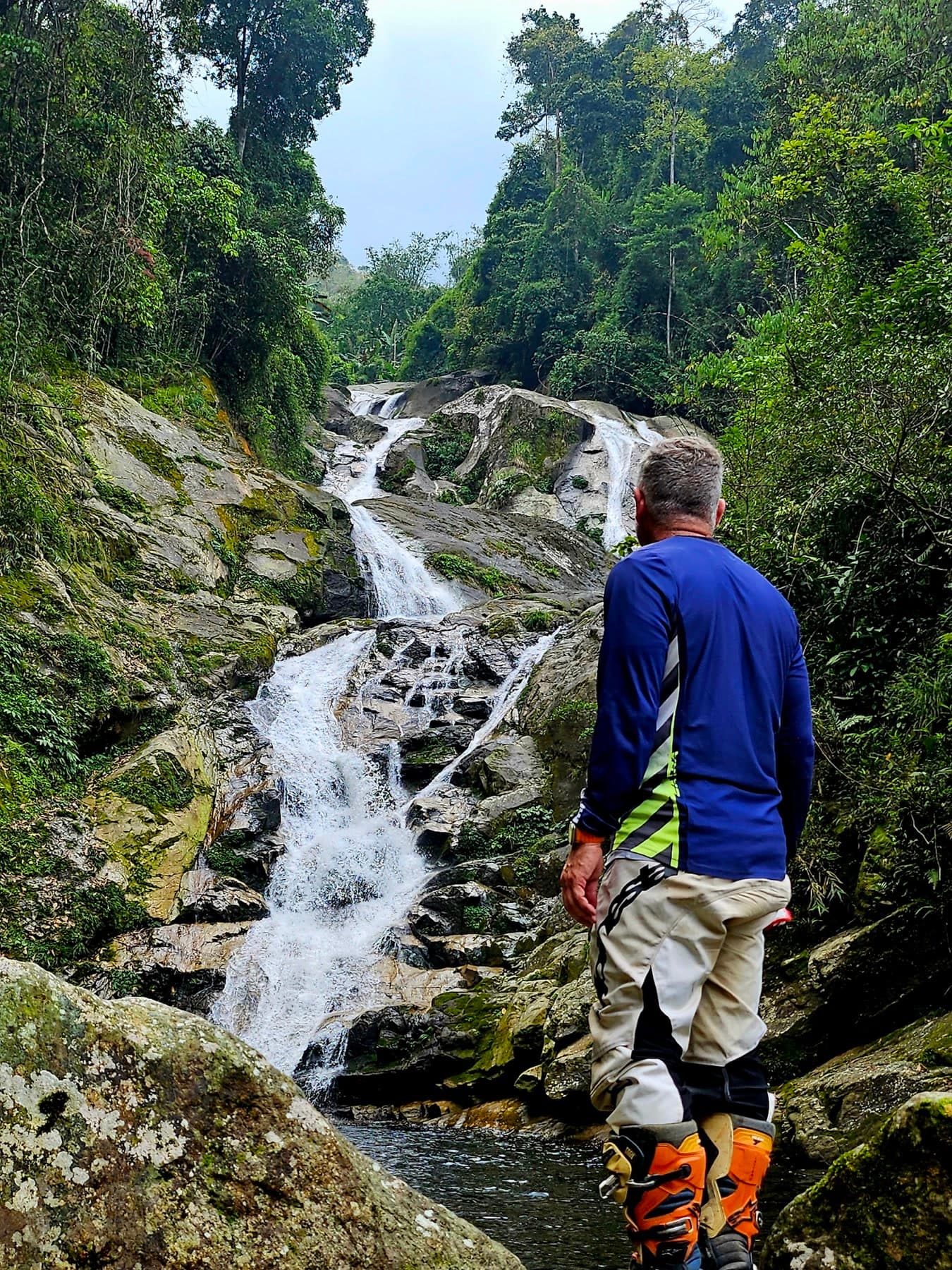A guest rider pausing to take in a jungle waterfall during a break on the Ha Giang Loop