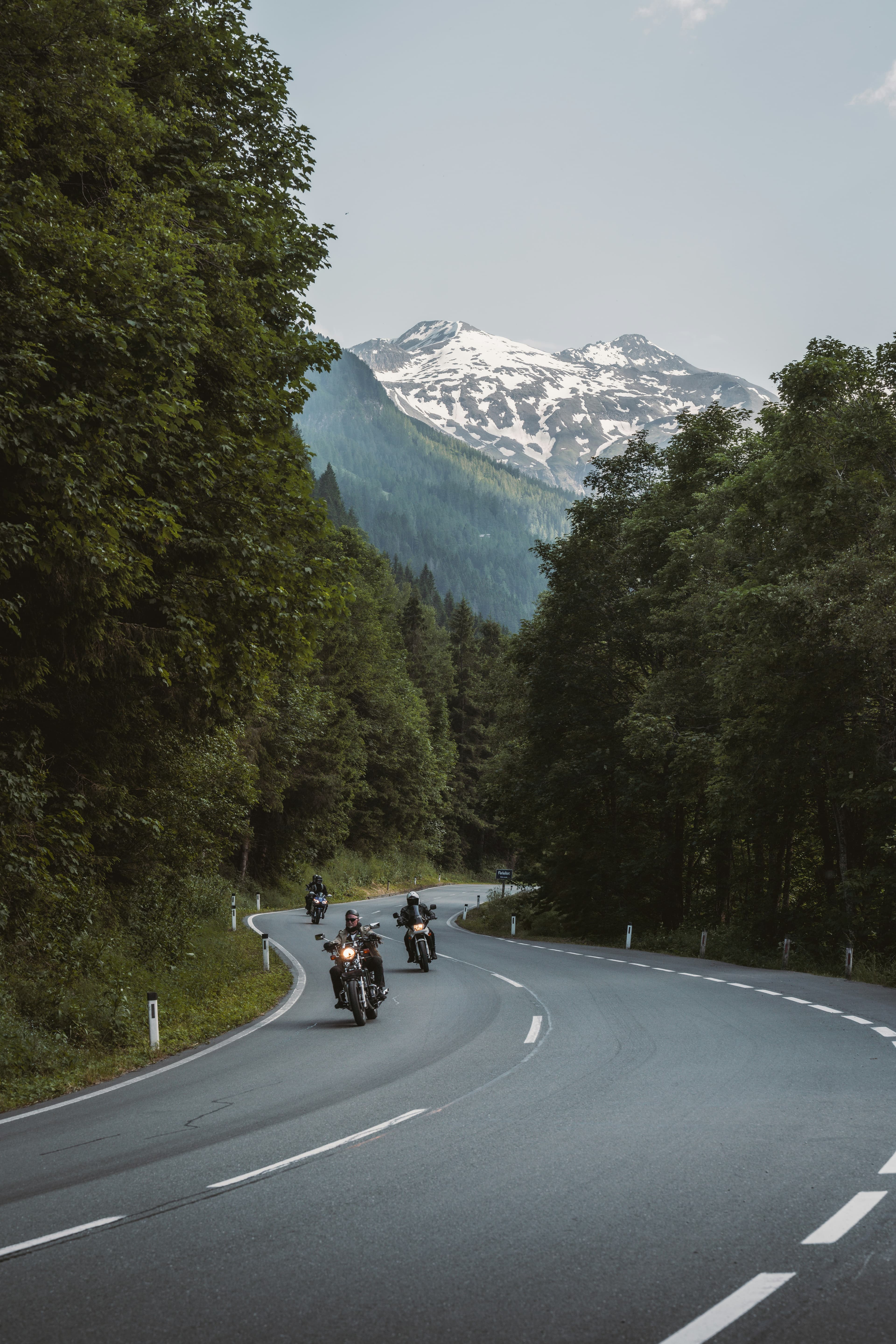 Riders on a mountain road with a high snow-streaked peak ahead