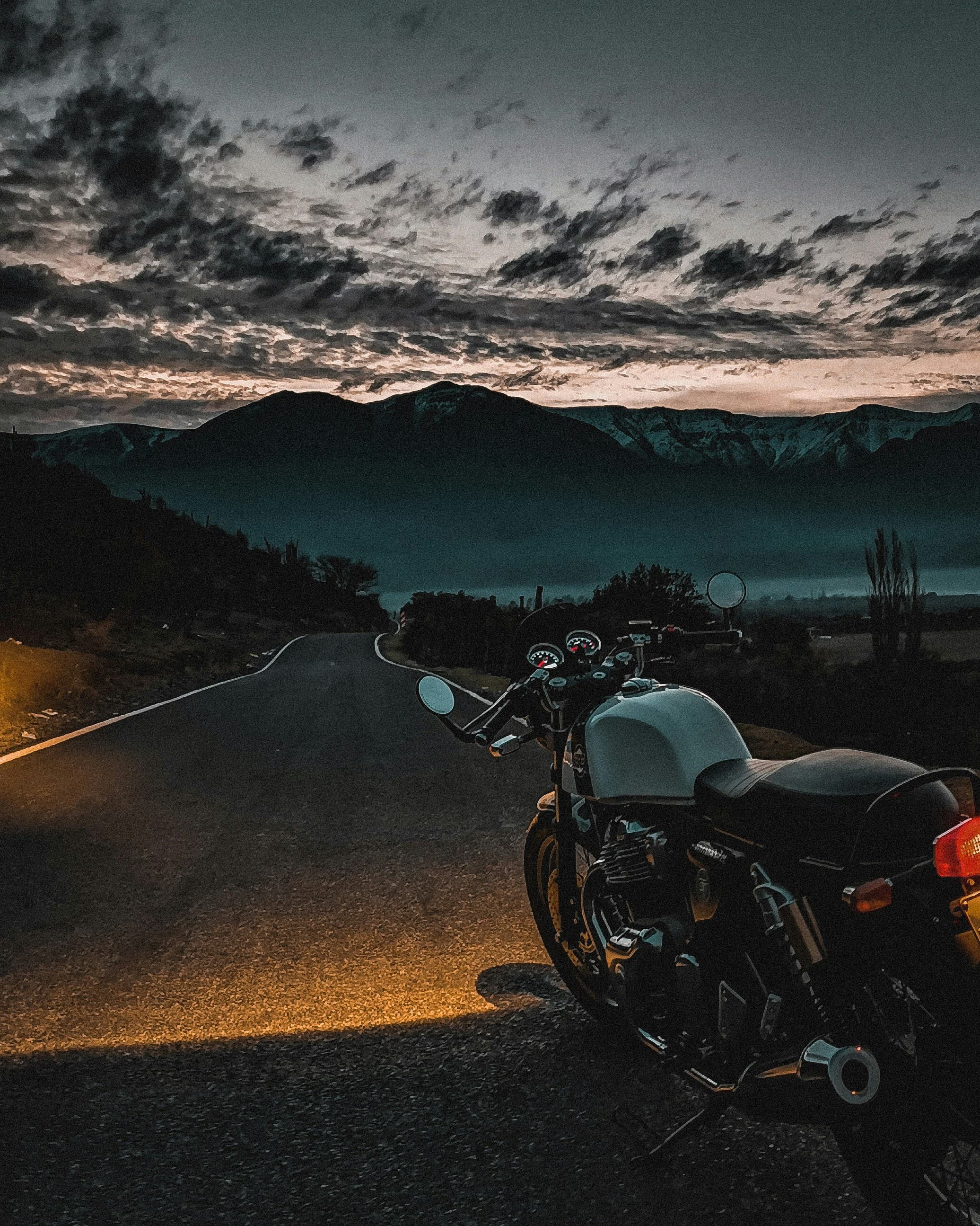 A motorbike at dusk on an empty road with mountains silhouetted behind