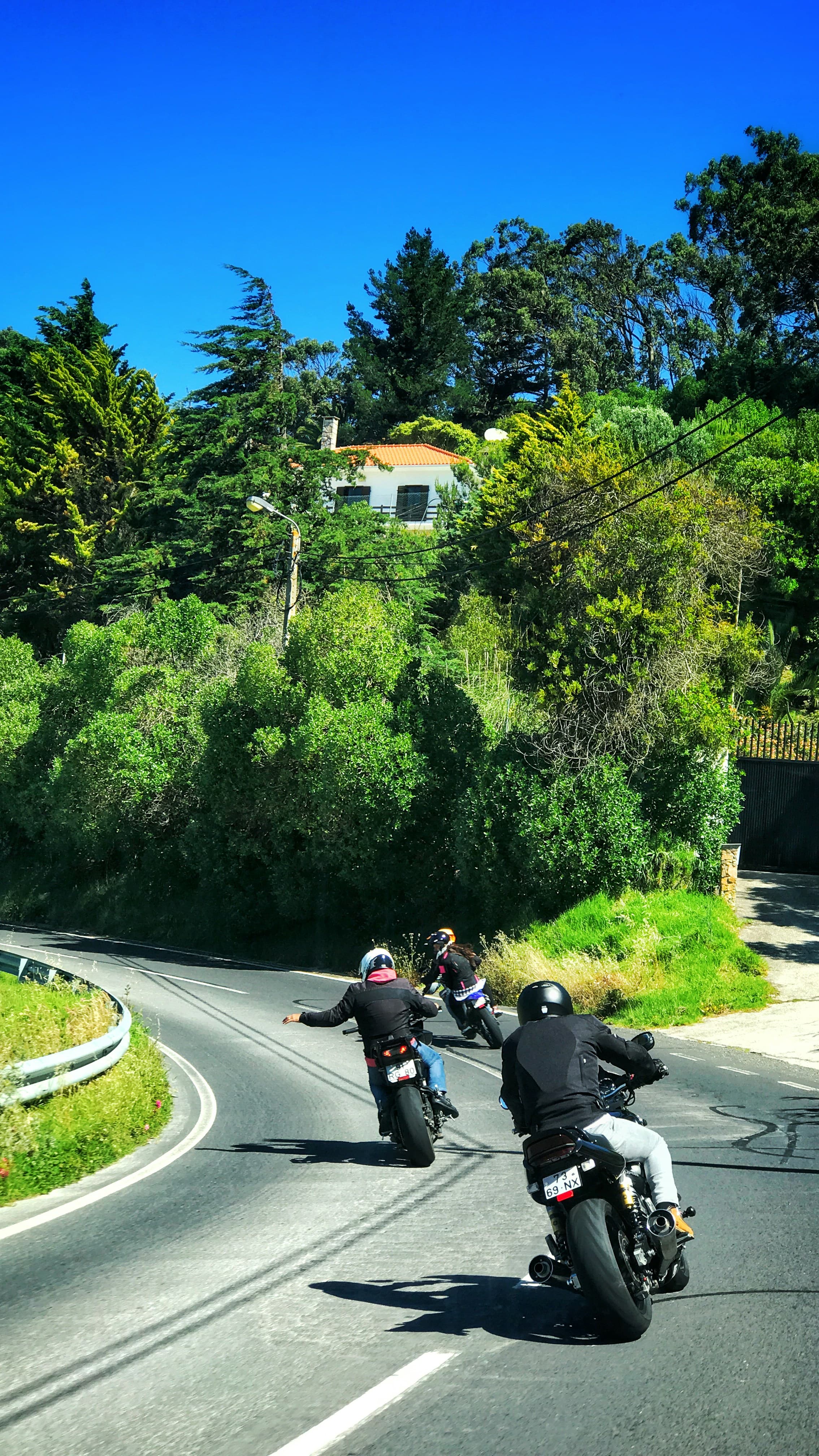 A group of riders cornering together on a sunlit mountain road